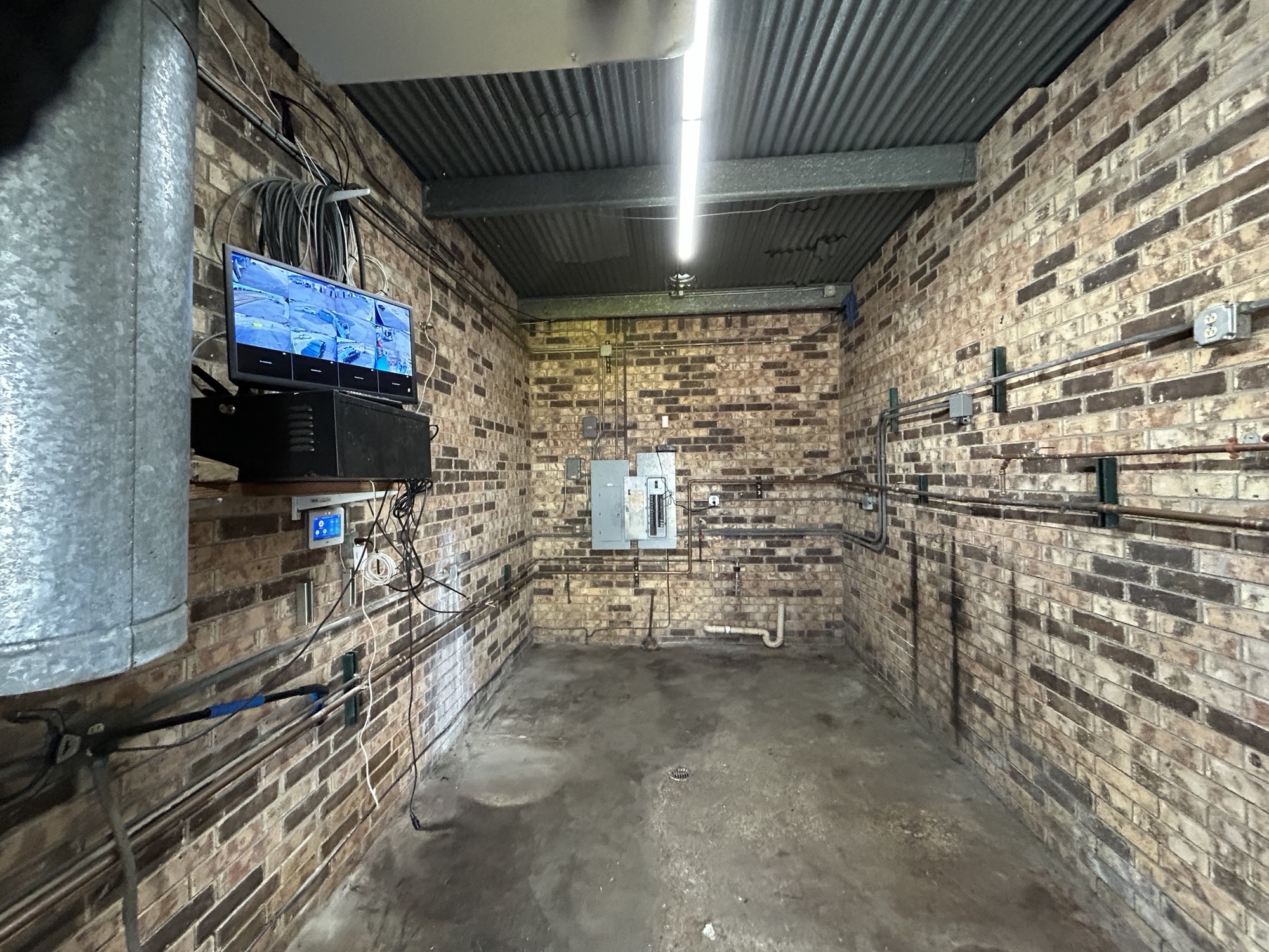 Carwash equipment room with electrical panels, plumbing, and surveillance monitor