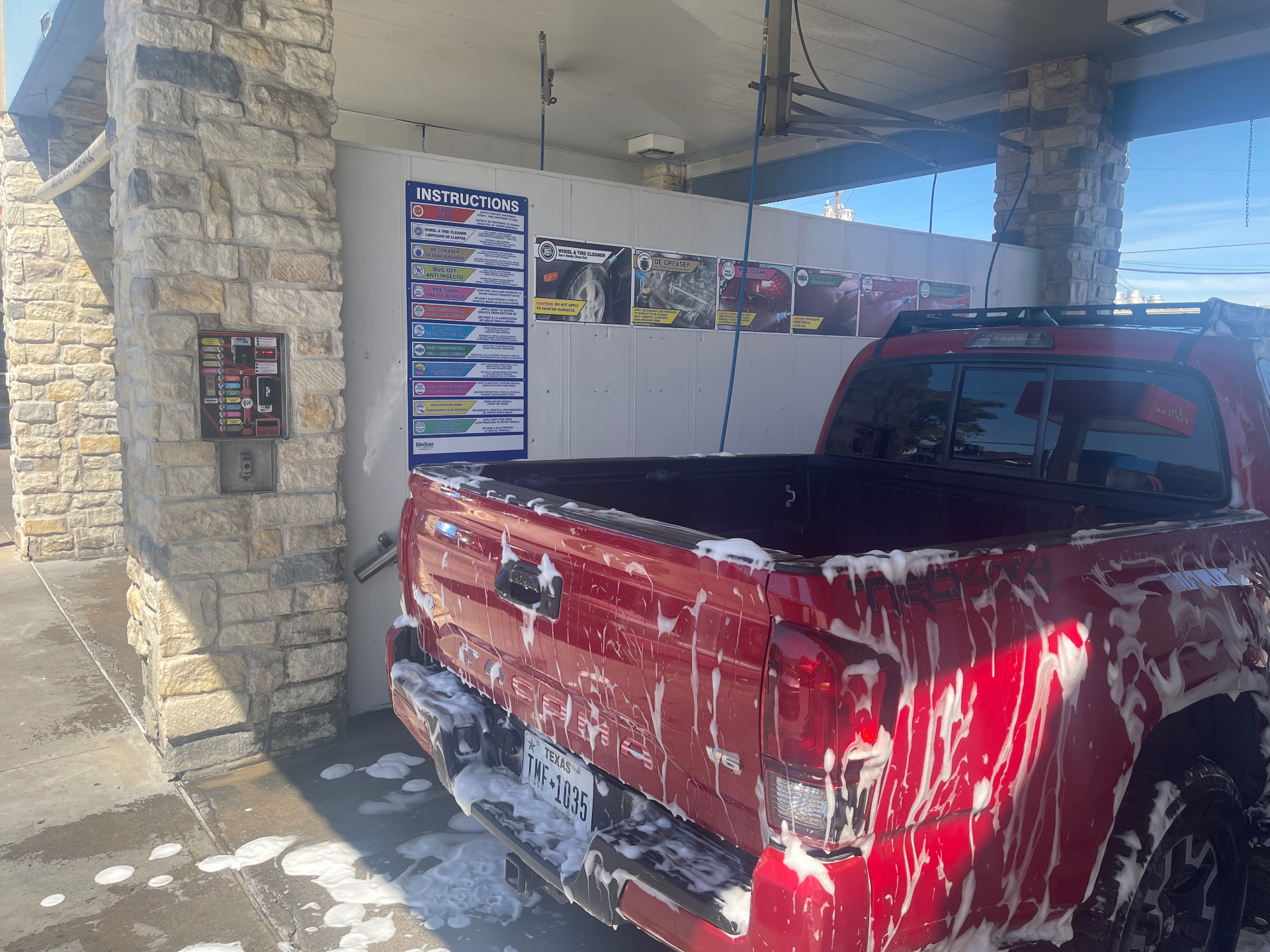 Red pickup truck covered in soap inside a self-serve carwash bay